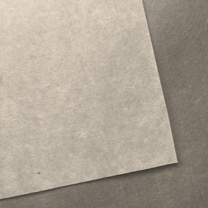 May include: Two pieces of textured paper, one beige and one light brown, are layered on top of each other. The beige paper is on top and is slightly angled.