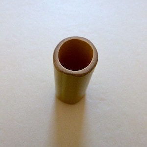May include: A natural bamboo tube with a smooth, light brown finish. The tube is open at the top and has a slightly rounded shape.