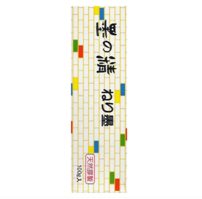 Puede incluir: Un paquete rectangular con un fondo de patr&oacute;n de ladrillos blancos y texto japon&eacute;s. El paquete tiene acentos coloridos de rojo, verde, azul y amarillo. El texto incluye las palabras "天然膠製" y "100g入".