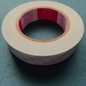 Pu&ograve; includere: Un rotolo di nastro adesivo a doppio lato bianco con testo blu e rosso che recita "SOOKWANG Made in Korea" e "1" Tape.