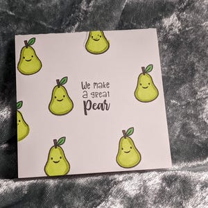May include: A white card with a pear design and the text "We make a great pear". The card is decorated with multiple cartoon pears with smiling faces.