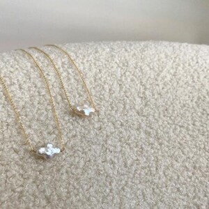 Puede incluir: Tres collares de cadena dorada con un colgante blanco de forma irregular. Los collares se exhiben sobre una superficie texturizada de color blanco roto. Los colgantes tienen una forma org&aacute;nica &uacute;nica, a&ntilde;adiendo un toque de elegancia a la joyer&iacute;a.