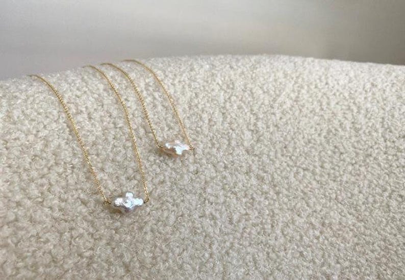 Puede incluir: Tres collares de cadena dorada con un colgante blanco de forma irregular. Los collares se exhiben sobre una superficie texturizada de color blanco roto. Los colgantes tienen una forma org&aacute;nica &uacute;nica, a&ntilde;adiendo un toque de elegancia a la joyer&iacute;a.