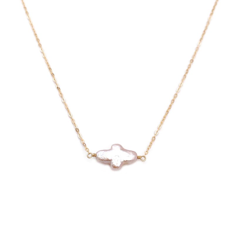 Puede incluir: Delicado collar de cadena dorada con un colgante de perla de forma irregular y color claro. El colgante tiene un brillo nacarado suave. El collar se muestra sobre un fondo blanco.