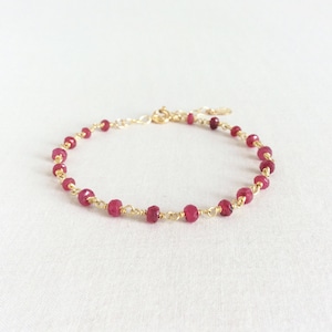 May include: A delicate gold chain bracelet with small, deep red ruby beads.