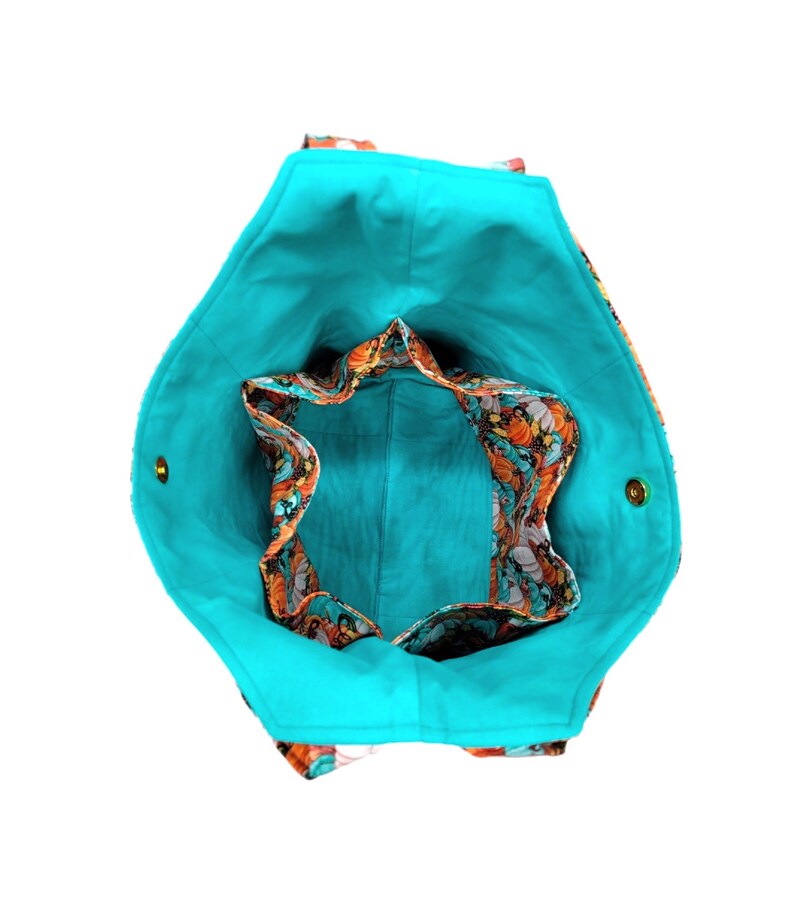 May include: A turquoise tote bag with a floral print lining. The bag has two gold-coloured buttons on the sides.