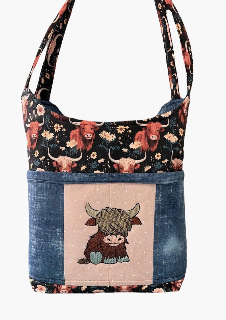 May include: A shoulder bag with a Highland cow theme. The top section features a black background with red-haired Highland cows and white flowers. The bottom is denim blue with a pink square embroidered with a cartoon Highland cow.
