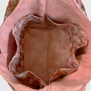 May include: Open view of a floral tote bag with a pink interior and multiple pockets. The bag's exterior features a muted floral pattern in shades of green, pink, and brown. The interior lining is a solid, soft pink. The bag has a structured design.