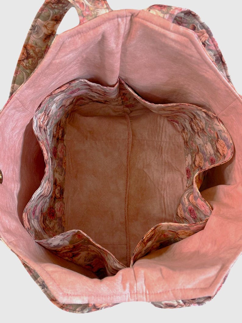 May include: Open view of a floral tote bag with a pink interior and multiple pockets. The bag's exterior features a muted floral pattern in shades of green, pink, and brown. The interior lining is a solid, soft pink. The bag has a structured design.