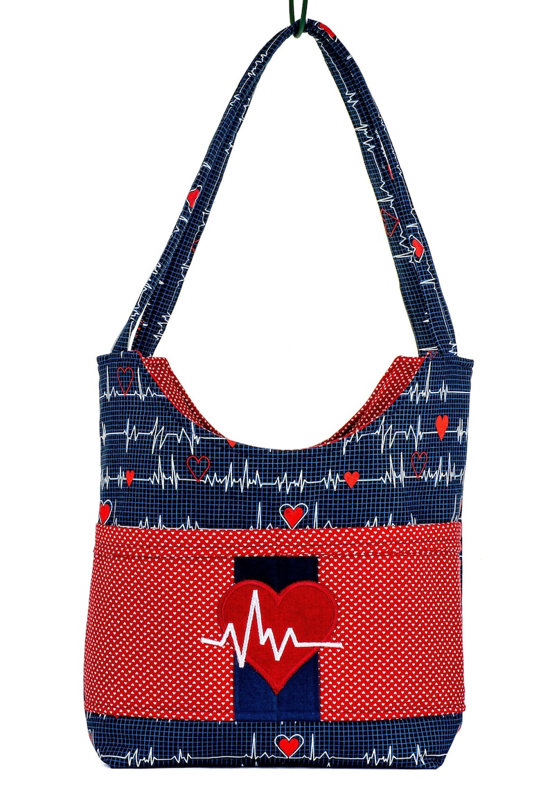 Peut inclure: Un sac fourre-tout bleu et rouge avec un motif de c&oelig;ur et d'ECG. Le sac a une grande poche sur le devant avec un c&oelig;ur rouge et un graphique ECG.