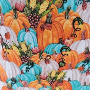 May include: A colourful fabric featuring a pattern of orange, white, and teal pumpkins. The pumpkins are arranged in a random pattern and are surrounded by green leaves, corn, and grapes.