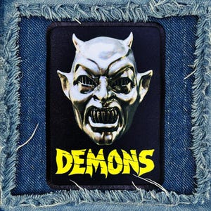 May include: A black patch with a silver demon head and the word "DEMONS" in yellow letters.