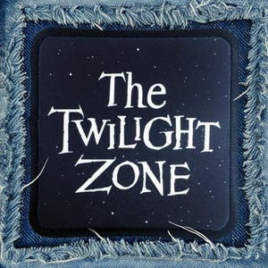 May include: A black patch with white text that reads "The Twilight Zone" on a denim background. The patch has a starry night sky design.