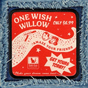 May include: A square fabric patch with a red background and black border, featuring the text ONE WISH WILLOW, AMAZE YOUR FRIENDS, and GET YOURS TODAY. The design includes a white graphic of a trail, two faces, stars, and a Tabi Cat logo.