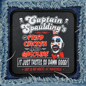 May include: A black and white patch with a cartoon image of a clown with a red, white, and blue hat. The text reads "Captain Spaulding's World Famous Fried Chicken and Gasoline It Just Tastes So Damn Good! Exit 13 Off Route I at Ruggsville."