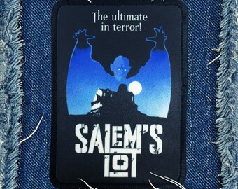 May include: A black and blue embroidered patch with the text "The ultimate in terror!" and "Salem's Lot" with a silhouette of a vampire with wings in front of a house.
