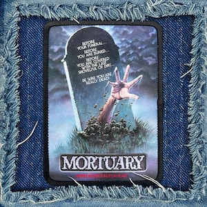 May include: A black and white patch with a hand reaching out of a grave. The text reads "Before your funeral... Before you are buried... Before you are covered with the last shovelful of dirt... Be sure you are really dead!" and "Mortuary Where Nobody Rests in Peace".