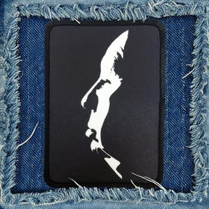 May include: Black and white silhouette of a person's face on a black fabric patch.
