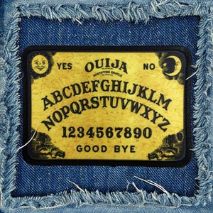 May include: A black and yellow fabric patch with the word "OUIJA" and the letters of the alphabet, numbers 1-9 and 0, and the words "YES", "NO", and "GOOD BYE".