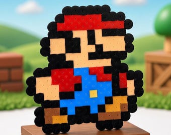 May include: A pixel art figure of a character wearing a red hat, red shirt, and blue overalls, constructed from small circular beads. The figure is mounted on a rectangular wooden base with a red panel, surrounded by several gold-colored coins.