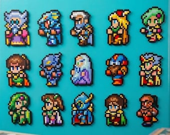 May include: A set of fifteen pixel art magnets arranged in three rows on a bright teal surface. Each magnet depicts a unique fantasy character with distinct colorful outfits, armor, and hairstyles, rendered in a classic 8-bit video game style.
