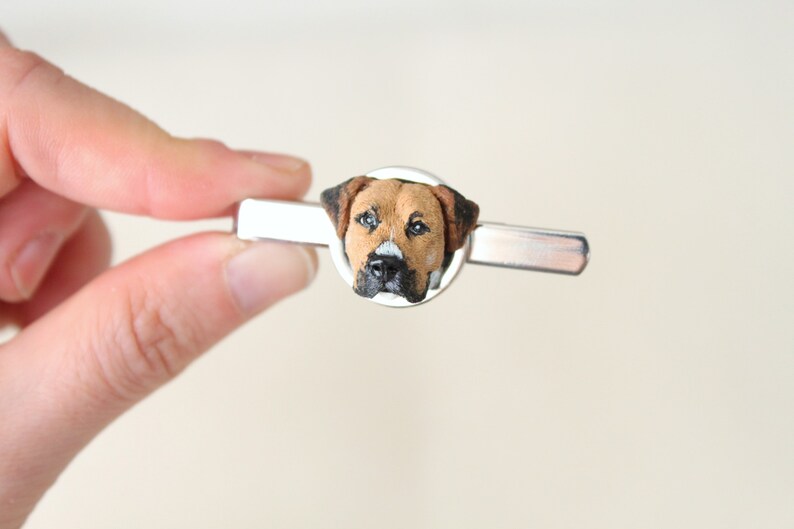 May include: A silver tie clip with a round, brown, black, and white dog head cameo.
