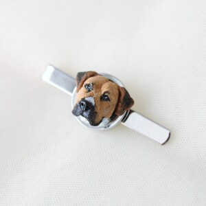 May include: A silver tie clip with a brown and white dog head sculpted in the center.