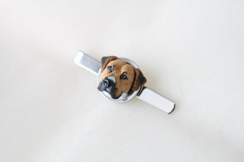 May include: A silver tie clip with a brown and white dog head sculpted in the center.