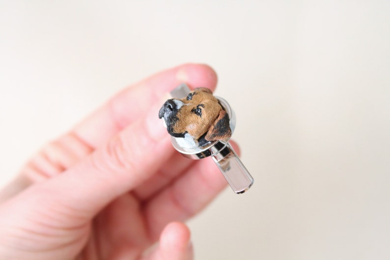 May include: A silver tie clip with a brown and white dog head sculpted on top.