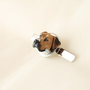 May include: A silver tie clip with a brown and white dog head sculpted in the center.