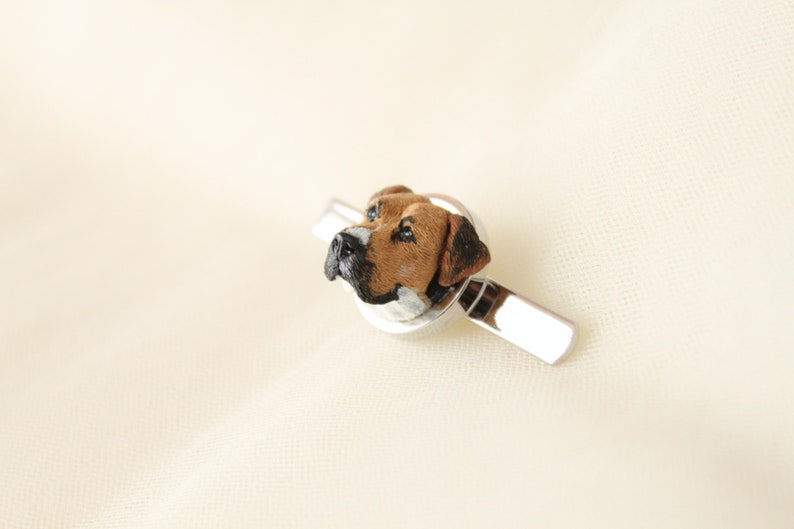 May include: A silver tie clip with a brown and white dog head sculpted in the center.