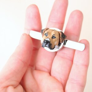 May include: A silver tie clip with a brown and black dog head sculpted on top.