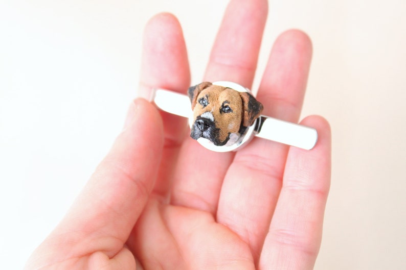 May include: A silver tie clip with a brown and black dog head sculpted on top.