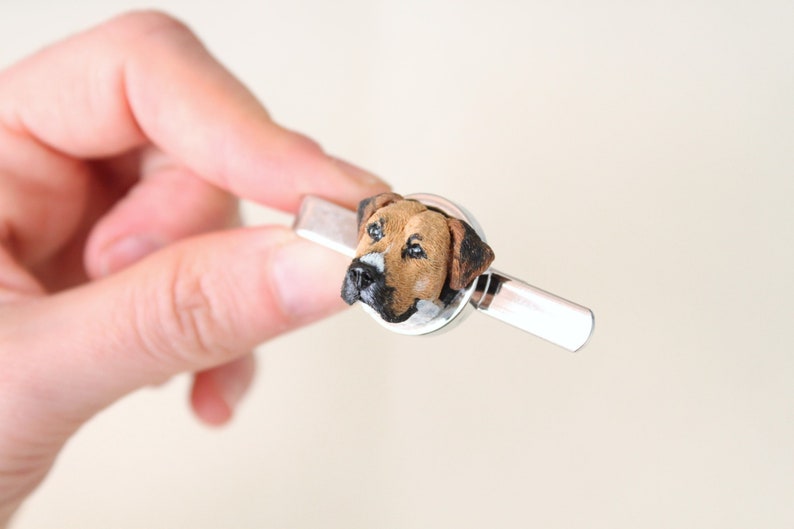 May include: A silver tie clip with a brown and black dog head sculpted on the front.