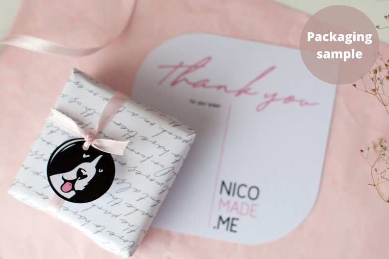 May include: A white gift box with a black and white dog illustration on a pink background. The box is tied with a pink ribbon. A white card with the text "Thank you" and "NICO MADE .ME" is on the right side of the image. The text "Packaging sample" is on the top right corner of the image.