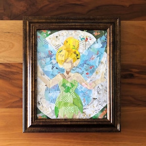 May include: Framed artwork featuring a collage of a fairy with yellow hair and a green dress. The fairy is set against a background of blue and white paper scraps. The frame is a dark brown color.