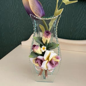 May include: A clear glass vase with a decorative floral design. The vase features a bouquet of purple, yellow, and white roses. The vase is perfect for displaying flowers or other decorative items.