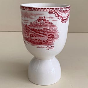 May include: White ceramic egg cup with a red transferware design featuring a castle scene and the text "Ludlow Castle in 1792". The egg cup has a rounded base and a flared top.