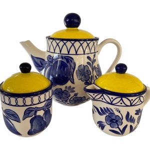 May include: A blue and white ceramic teapot, creamer, and sugar bowl set with yellow lids. The set features a floral design with blue flowers and leaves on a white background.