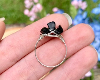 May include: A silver wire wrapped ring with black gemstone accents. The ring is on a hand, with the stones facing the camera.