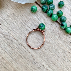 Könnte beinhalten: Ein Ring aus Kupferdraht mit einem grünen Edelstein, der um das Band gewickelt ist.