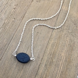 Puede incluir: Un collar de cadena plateada con un colgante de piedra de lava ovalada negra.