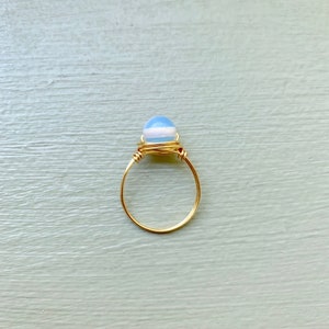 May include: A gold wire wrapped ring with a light blue and white opal gemstone.