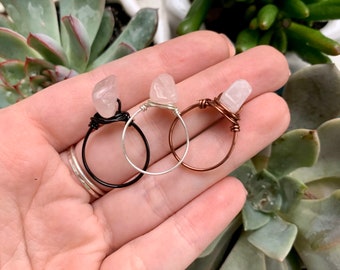 May include: Three wire-wrapped rings with clear quartz stones. The rings are made with black, silver, and copper wire.