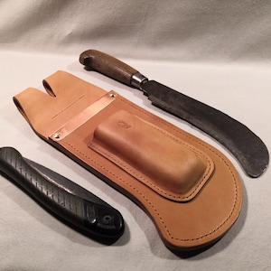 May include: A tan leather tool belt with a pocket for a small saw and a larger pocket for a curved blade. The belt has a copper-colored metal plate on the front.