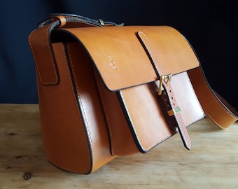 May include: A tan leather messenger bag with a buckle closure and a long strap. The bag has a flap that closes with a buckle.