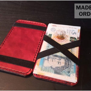 May include: A red leather wallet with a black elastic band to hold cash. The wallet is open and has several British five pound notes inside. The text "MADE TO ORDER" is visible in the top right corner of the image.