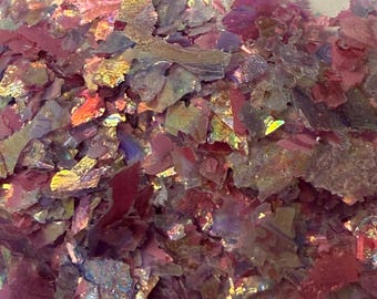 Puede incluir: Primer plano de escamas iridiscentes multicolores. Las escamas son principalmente tonos de rosa, rojo y dorado, con una calidad brillante y reflectante. La textura parece irregular y fragmentada, creando un efecto visual dinámico.