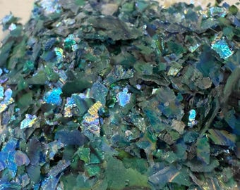 Puede incluir: Un montón de escamas iridiscentes trituradas en tonos de verde azulado, azul y verde. Las escamas tienen una cualidad reflectante y brillante, que atrapa la luz para crear un efecto brillante. El material parece ser un suministro de artesanía decorativa.