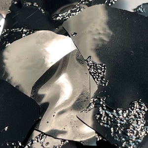 May include: Close-up of a pile of black and silver metallic flakes. The flakes are irregularly shaped and have a shiny, reflective surface.